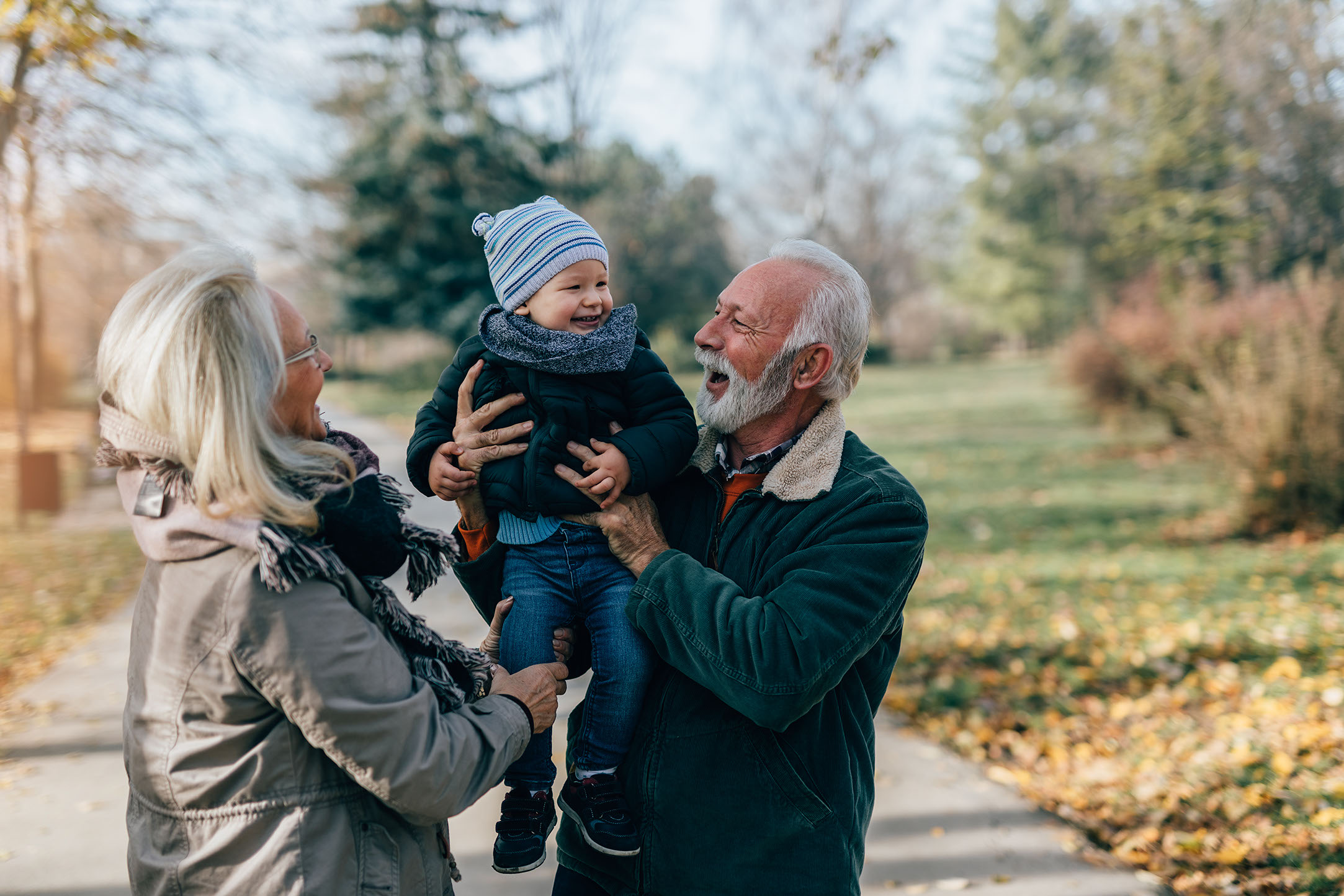 Lykkelig, pent eldre par, ektemann og kone, går og leker med sitt bedårende barnebarn i offentlig bypark.